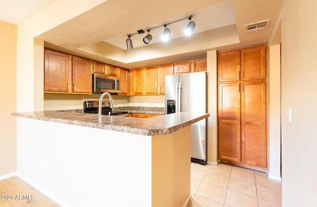 kitchen with kitchen peninsula, stainless steel appliances, light tile patterned floors, and track lighting