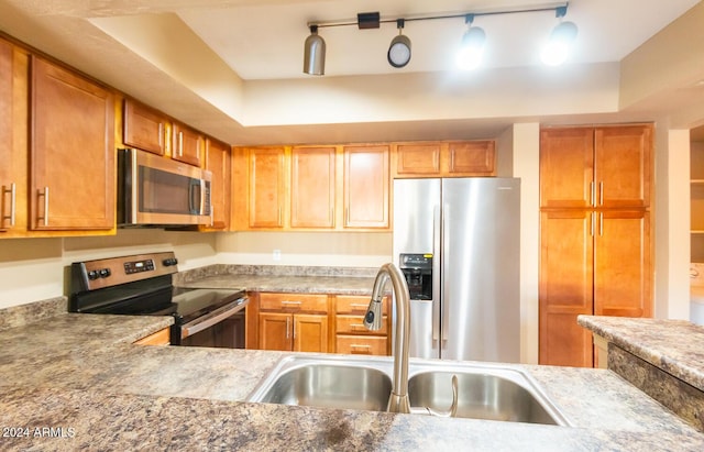 kitchen with a tray ceiling, sink, appliances with stainless steel finishes, and track lighting