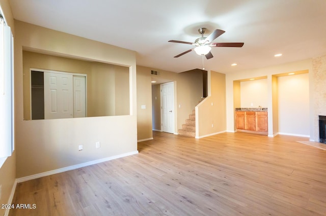 unfurnished living room with a large fireplace, ceiling fan, and light hardwood / wood-style flooring