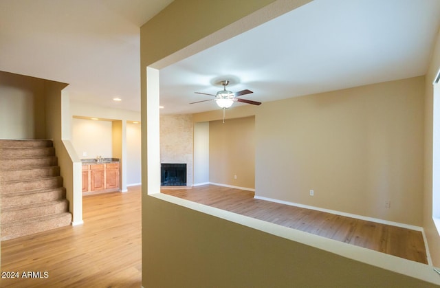 unfurnished living room with a large fireplace, light hardwood / wood-style flooring, ceiling fan, and sink