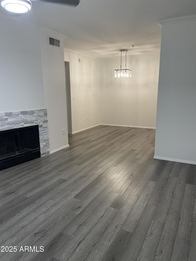 unfurnished living room with visible vents, ornamental molding, a stone fireplace, dark wood-style floors, and a notable chandelier