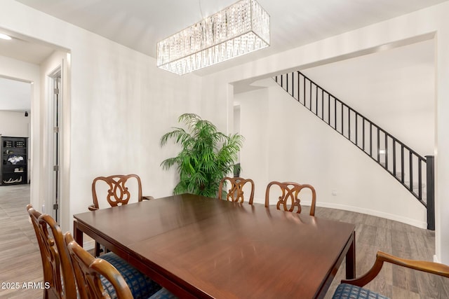 dining space with baseboards, stairway, a chandelier, and wood finished floors