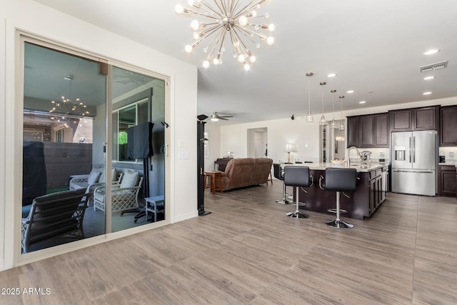 interior space with an inviting chandelier, a sink, dark brown cabinetry, open floor plan, and stainless steel refrigerator with ice dispenser