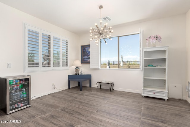unfurnished room with beverage cooler, wood finished floors, a healthy amount of sunlight, and an inviting chandelier