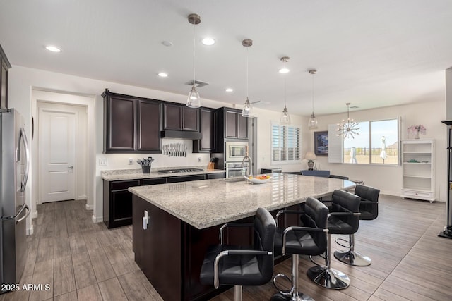 kitchen featuring light stone counters, visible vents, wood finished floors, stainless steel appliances, and a kitchen island with sink