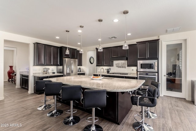 kitchen with light stone counters, visible vents, a sink, a kitchen breakfast bar, and stainless steel appliances