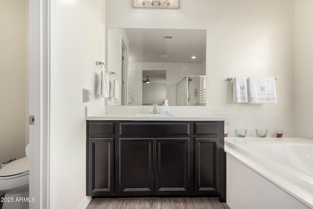 bathroom featuring toilet, wood finished floors, vanity, visible vents, and a stall shower