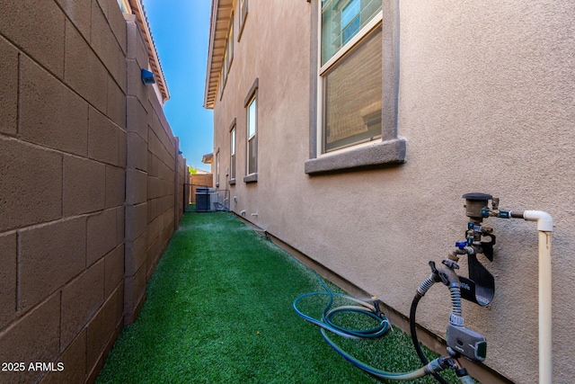 view of property exterior featuring a lawn, central AC unit, stucco siding, and fence