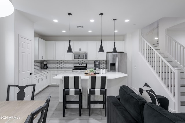 kitchen featuring tasteful backsplash, stainless steel appliances, white cabinetry, decorative light fixtures, and a center island