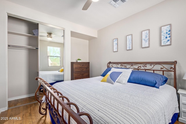 bedroom with a ceiling fan, wood finished floors, visible vents, baseboards, and a closet