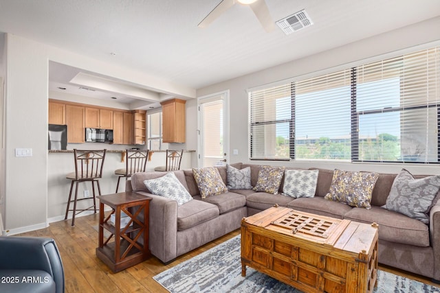 living room with visible vents, baseboards, ceiling fan, and light wood finished floors