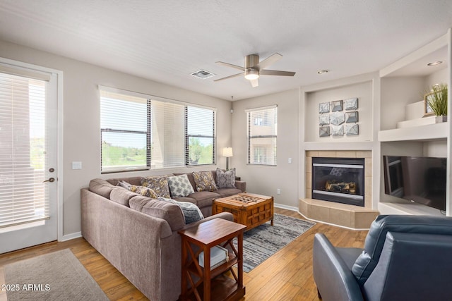 living room featuring wood finished floors, a ceiling fan, visible vents, baseboards, and a fireplace