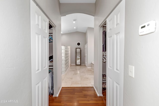 hallway featuring arched walkways, vaulted ceiling, light wood-type flooring, and baseboards