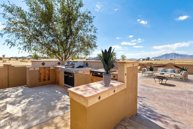 view of patio / terrace with an outdoor kitchen, a mountain view, a fire pit, area for grilling, and fence