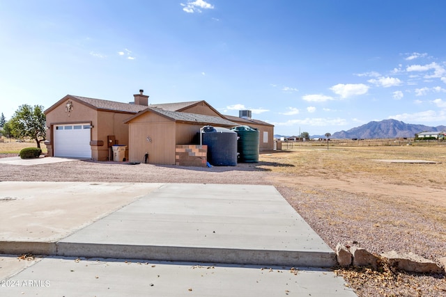 exterior space featuring an attached garage, a mountain view, concrete driveway, stucco siding, and a chimney