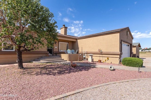 ranch-style home with an attached garage, a chimney, and stucco siding