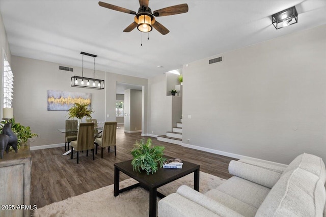 living room with stairs, wood finished floors, visible vents, and a ceiling fan