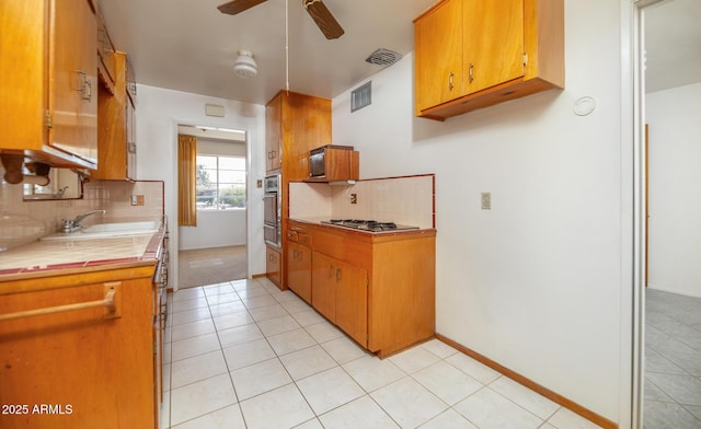 kitchen featuring visible vents, a sink, ceiling fan, stainless steel appliances, and tile counters