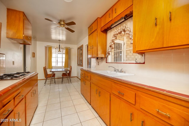 kitchen featuring ceiling fan with notable chandelier, a sink, light tile patterned floors, decorative backsplash, and stainless steel gas cooktop