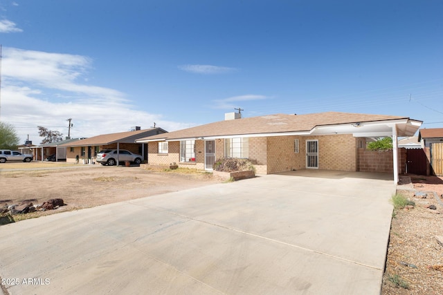 view of front facade featuring an attached carport, concrete driveway, brick siding, and fence