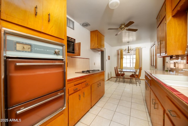 kitchen with light tile patterned floors, visible vents, oven, tile counters, and ceiling fan with notable chandelier