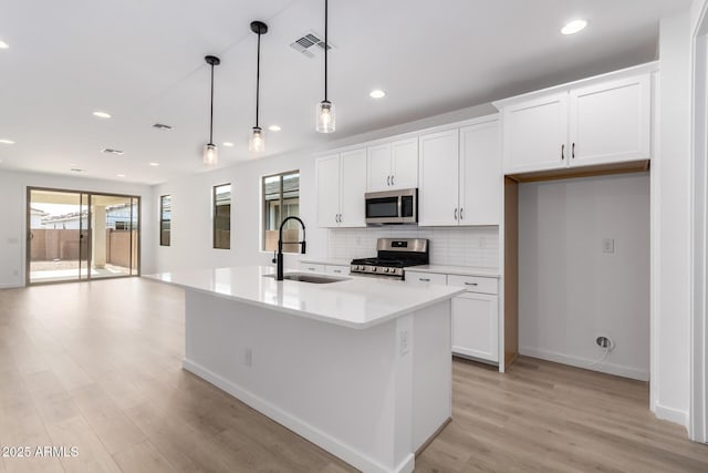 kitchen featuring decorative light fixtures, white cabinetry, sink, a kitchen island with sink, and stainless steel appliances