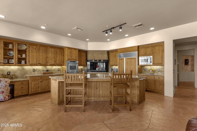 kitchen with built in appliances, brown cabinetry, tasteful backsplash, a breakfast bar, and visible vents