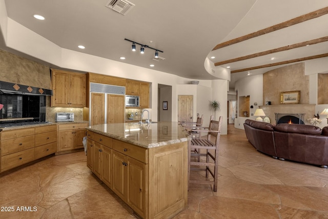 kitchen with built in appliances, a sink, visible vents, open floor plan, and a kitchen breakfast bar