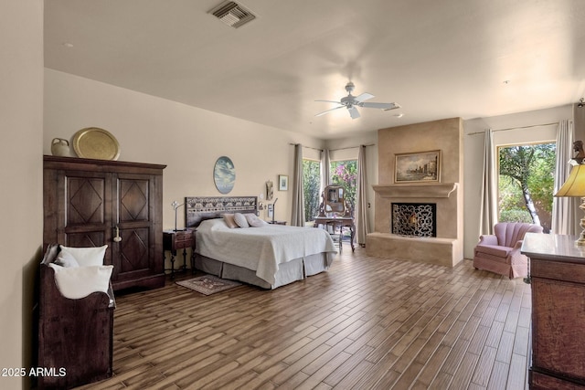 bedroom featuring a fireplace with raised hearth, visible vents, wood finished floors, and multiple windows