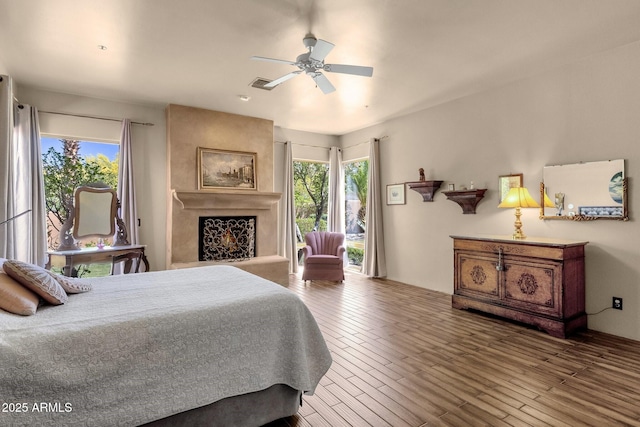 bedroom with wood finished floors, a large fireplace, a ceiling fan, and visible vents