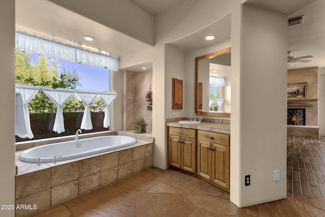 bathroom featuring a large fireplace, visible vents, a garden tub, vanity, and a ceiling fan