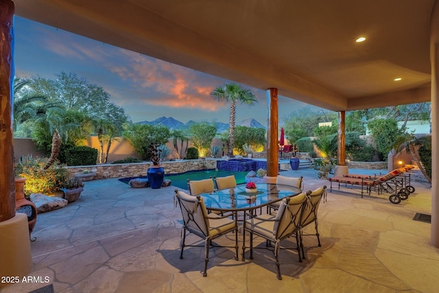 patio terrace at dusk with a mountain view, outdoor dining space, and a fenced backyard