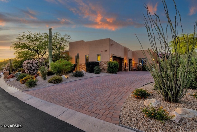 pueblo-style house with stucco siding, decorative driveway, stone siding, and a garage