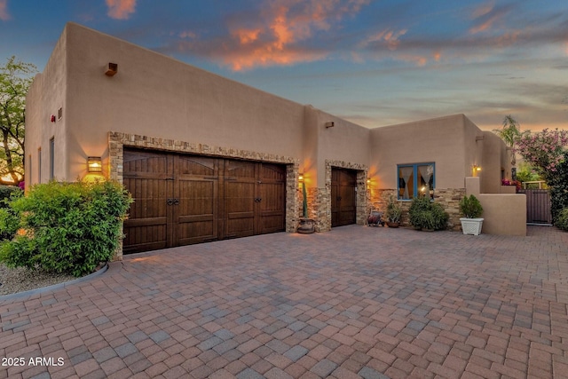 southwest-style home featuring a garage, stucco siding, decorative driveway, and stone siding