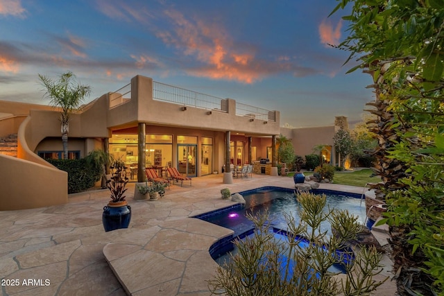 back of house at dusk featuring stucco siding, an outdoor pool, and a patio area