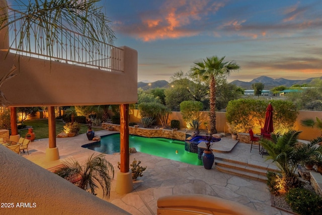 pool at dusk featuring a pool with connected hot tub, a mountain view, a fenced backyard, and a patio area