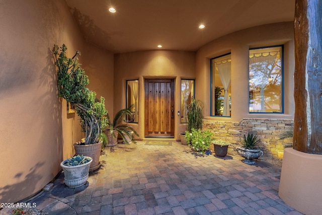 property entrance featuring stucco siding, a patio, and stone siding