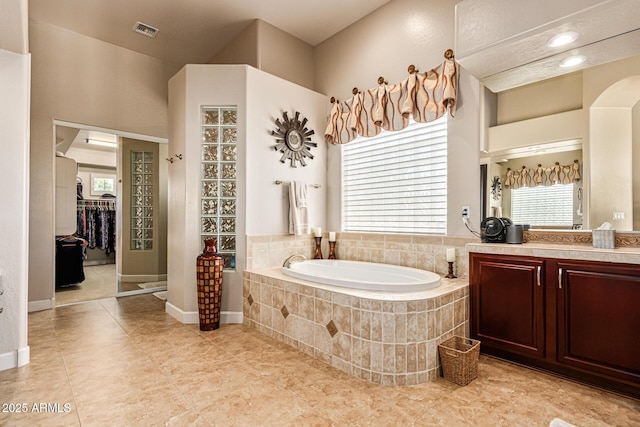 bathroom featuring tile patterned flooring, vanity, and a relaxing tiled tub