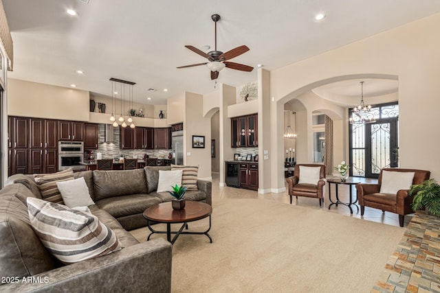 carpeted living room with ceiling fan with notable chandelier and a high ceiling