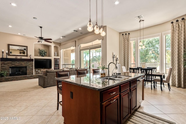 kitchen with dishwasher, an island with sink, sink, hanging light fixtures, and light tile patterned floors