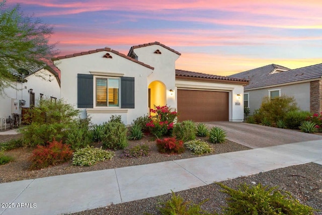 mediterranean / spanish-style home featuring a tiled roof, decorative driveway, an attached garage, and stucco siding