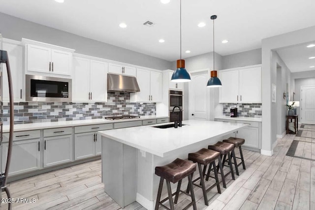 kitchen with appliances with stainless steel finishes, wood tiled floor, a sink, and under cabinet range hood