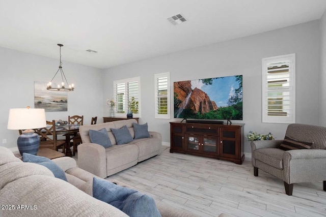 living room featuring light wood-style floors, visible vents, a notable chandelier, and baseboards