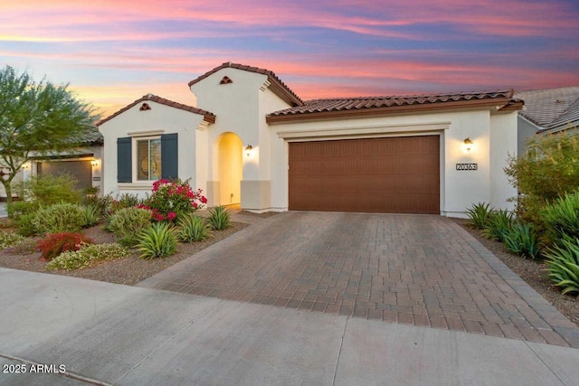 mediterranean / spanish-style home featuring an attached garage, a tile roof, decorative driveway, and stucco siding