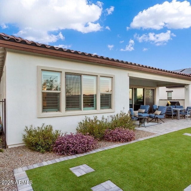 rear view of house featuring a patio, a yard, a tile roof, and stucco siding