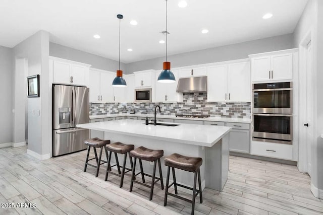 kitchen featuring under cabinet range hood, a sink, appliances with stainless steel finishes, decorative backsplash, and an island with sink