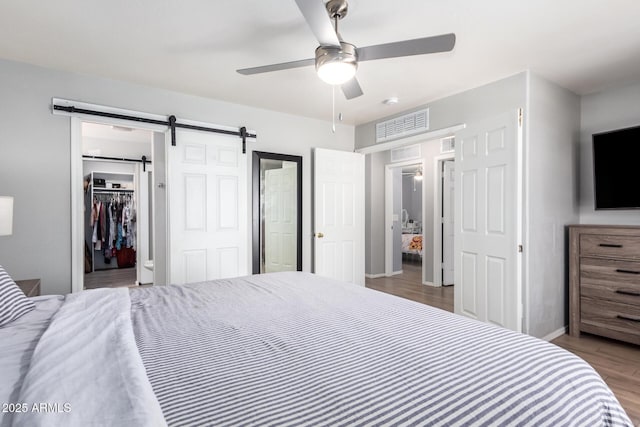 bedroom with a spacious closet, visible vents, baseboards, a barn door, and wood finished floors
