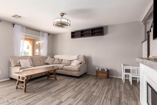 living room featuring visible vents, baseboards, light wood-style floors, and a fireplace