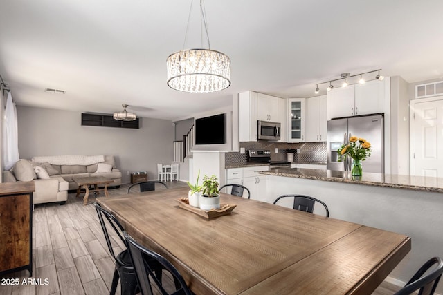 dining space with track lighting, wood finish floors, visible vents, and a chandelier