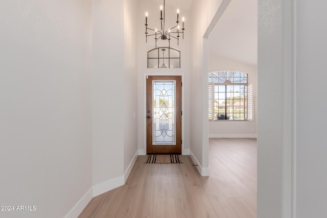 foyer entrance featuring a notable chandelier, light wood-type flooring, and vaulted ceiling